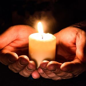 Close up photo of two hands cradling a white candle. The background is black.
