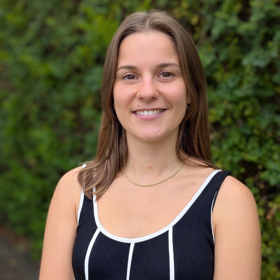 Photo of Natalie, a young woman with medium length brown hair. She is smiling at camera and wearing a sleeveless black top.