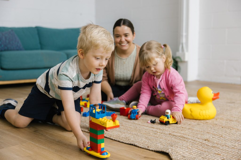 A mum and her two children sit on the floor playing with blocks.
