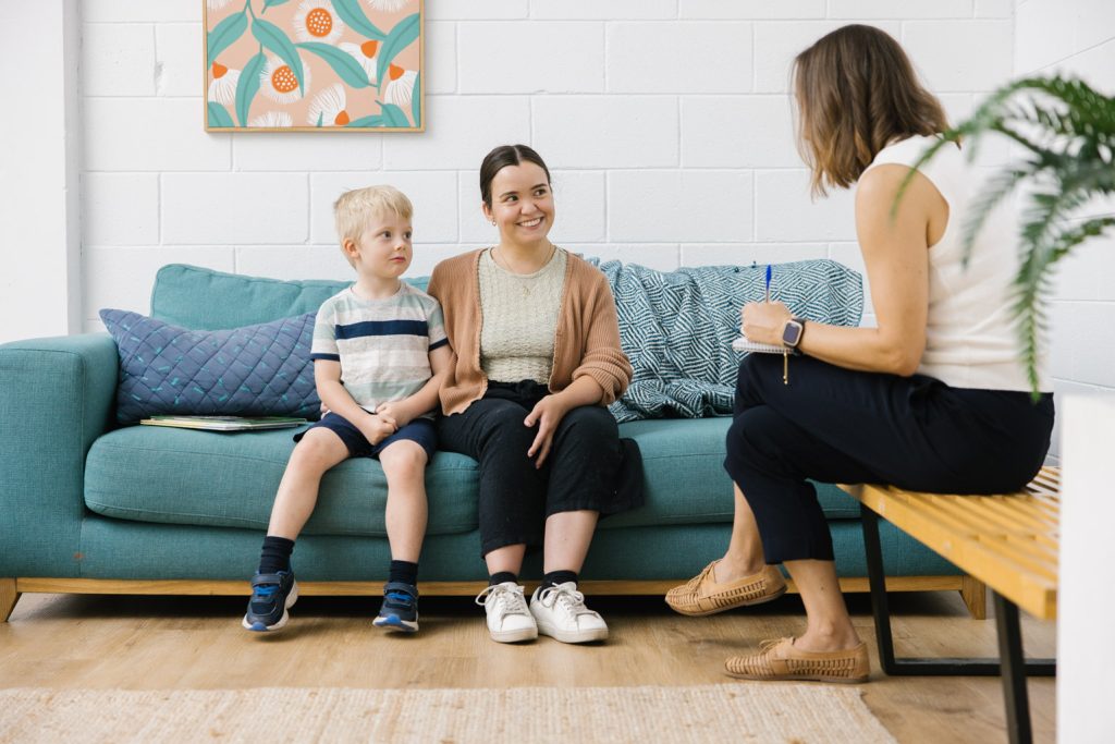 A mother and child are sitting on a blue sofa, talking to a health professional.
