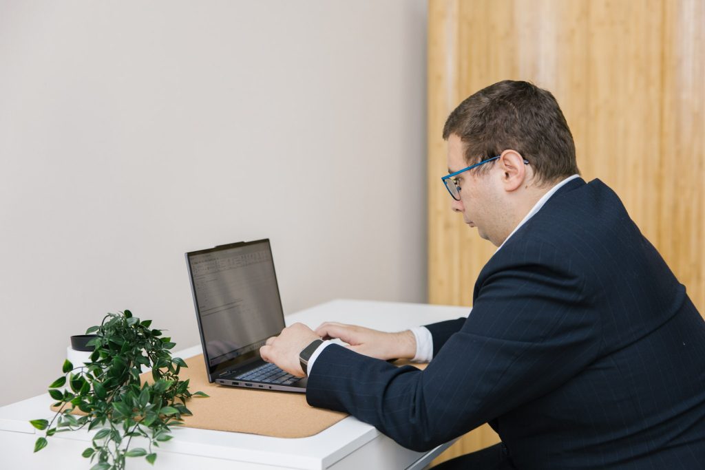 A person with short brown hair is sitting at a laptop computer at a desk.