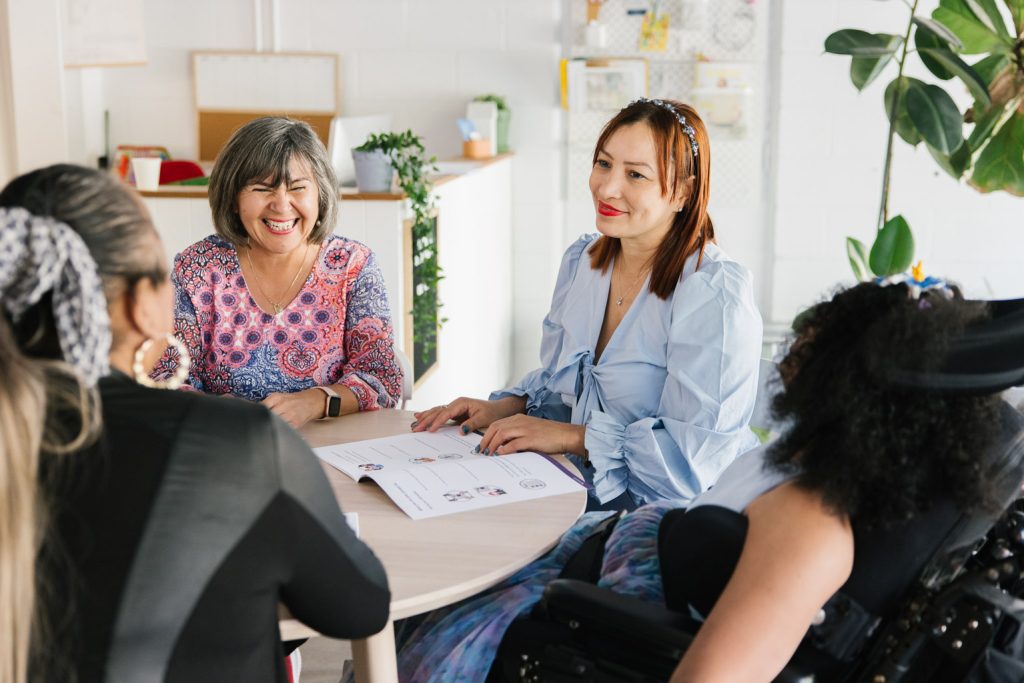 A group of people from a Spanish-speaking background sitting at a table, talking to each other and smiling.