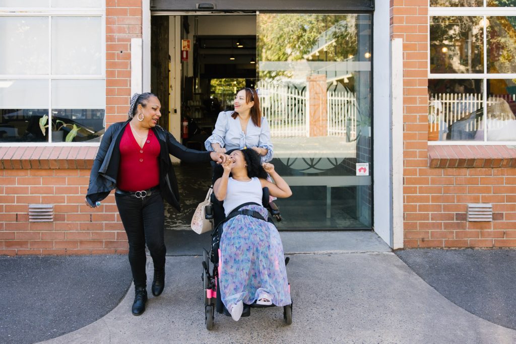 Three people are walking out of a building. One person is using a wheelchair.