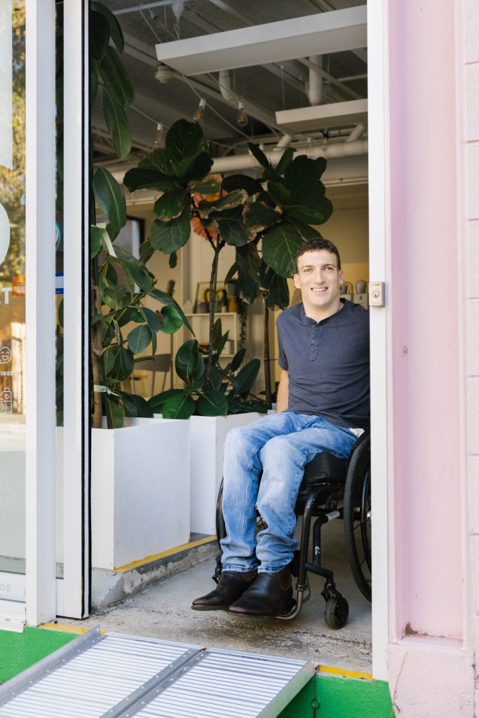 A man using a wheelchair is exiting a door and using a ramp.