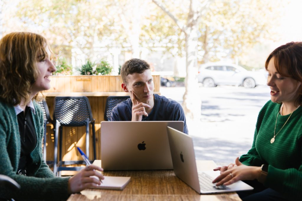 Three people sit around a table, using laptop computers.
