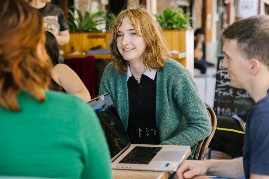 Three people are sitting at a cafe table and talking to one another.
