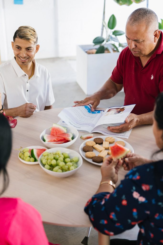 People from a Bhutanese community sit around a table talking and sharing food