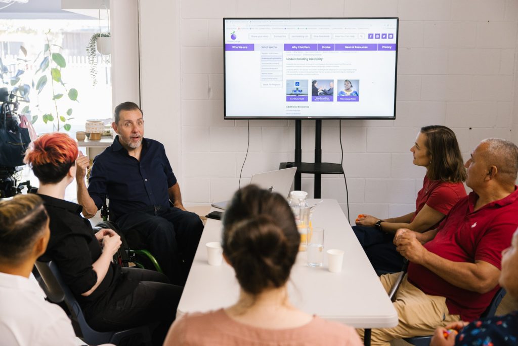 A person using a wheelchair is delivering a training session to a group of people
