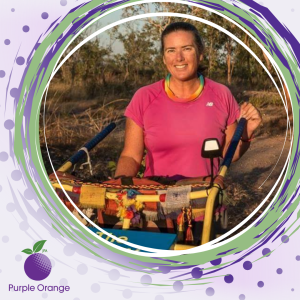 light purple background with spots. dark purple circle with dusty purple, light green and white swirling accents. Photo of Terra smiling during the trek around Australia wearing a pink shirt and wheeling a trolley. Nature in the background of the photo.