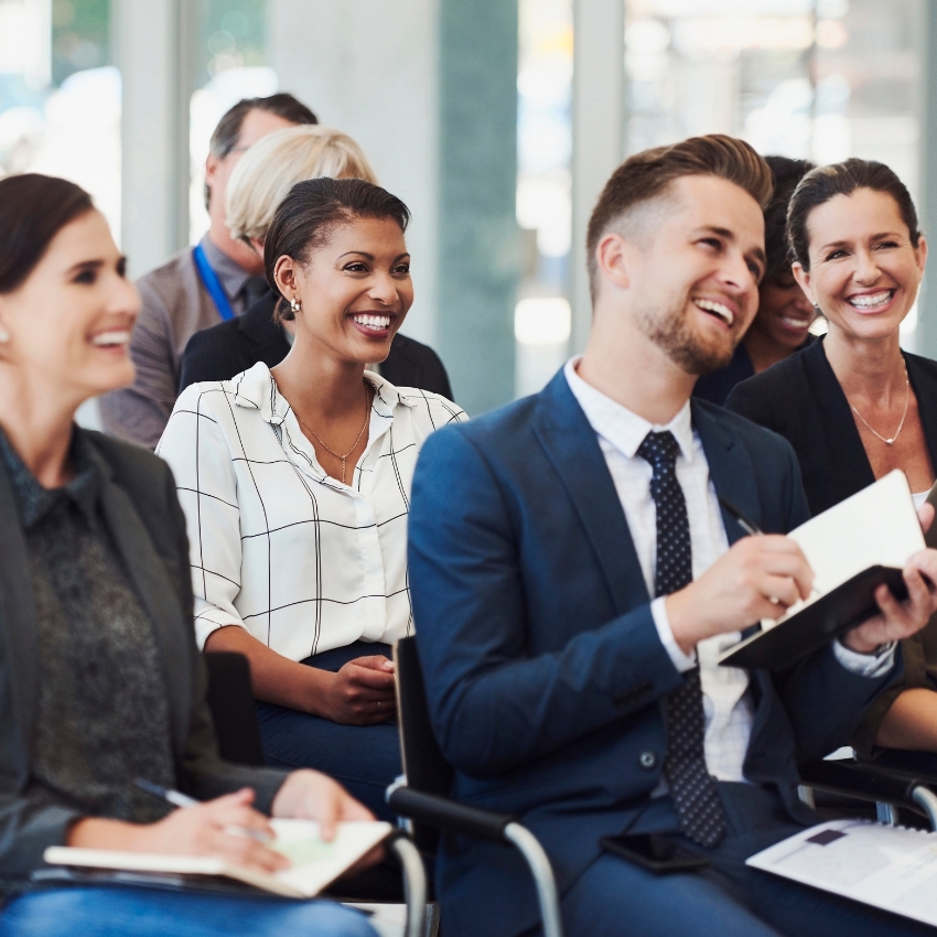 A group of seated men and women in business attire are smiling and looking ahead.